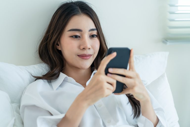 Asian attractive woman use mobile phone chat on bed at home in morning.